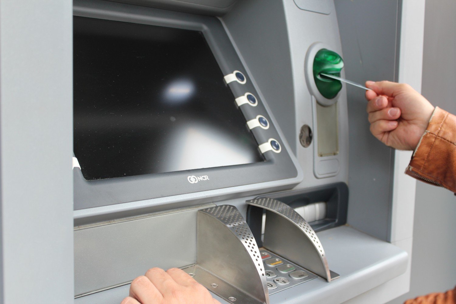 Person using an ATM with card slot, keypad and screen, representing banking access in Kalkan.