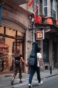 People walking past a Turkish pharmacy with red flags and a prominent illuminated pharmacy sign.