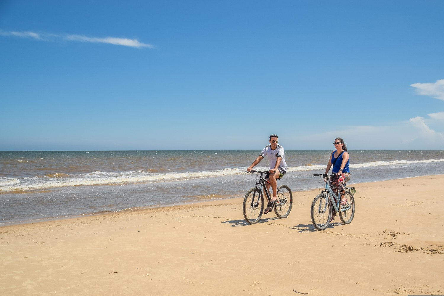 Two people cycling along a sandy beach shoreline, showing eco‑friendly transport options for getting around Kalkan.