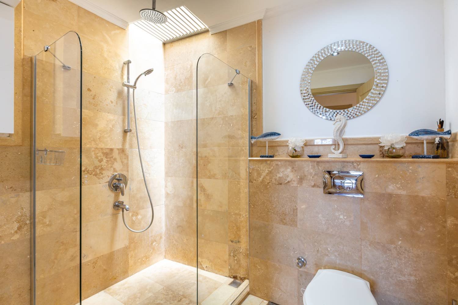 Modern bathroom at Kalkan Limon Apartment with marble tiles, walk‑in shower and decorative shelf.