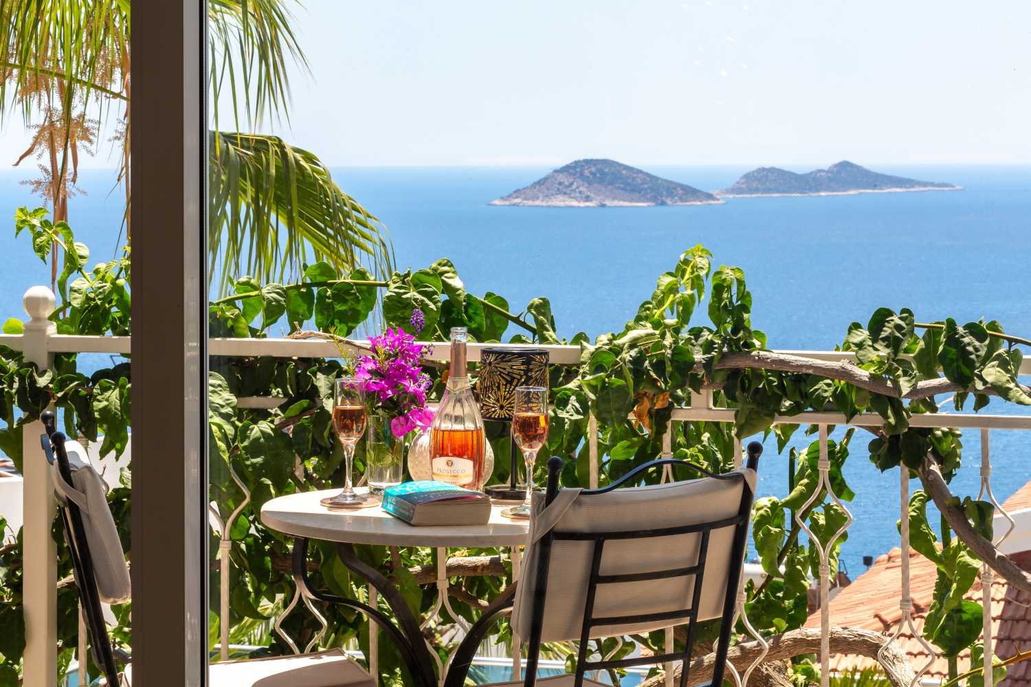 Balcony at Kalkan Limon Apartment with sea views, wine glasses and coastal greenery.