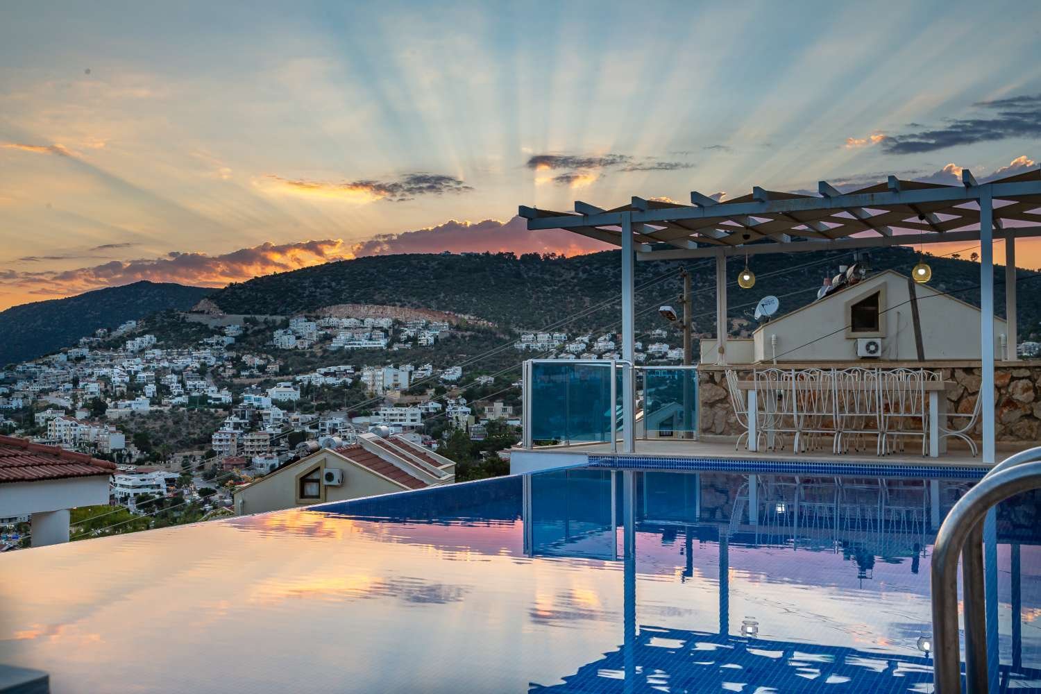 Sunset view from Kalkan Limon Apartment overlooking infinity pool, hillside town and mountains.