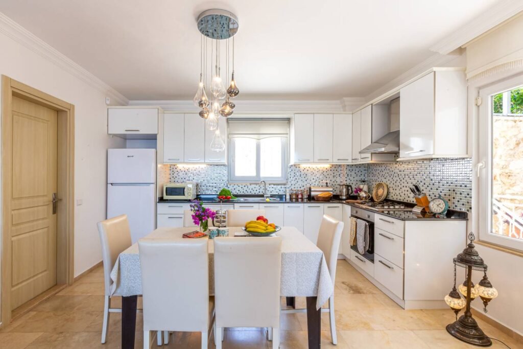 Modern kitchen and dining area at Kalkan Limon Apartment with white cabinetry, mosaic backsplash and a decorated dining table.