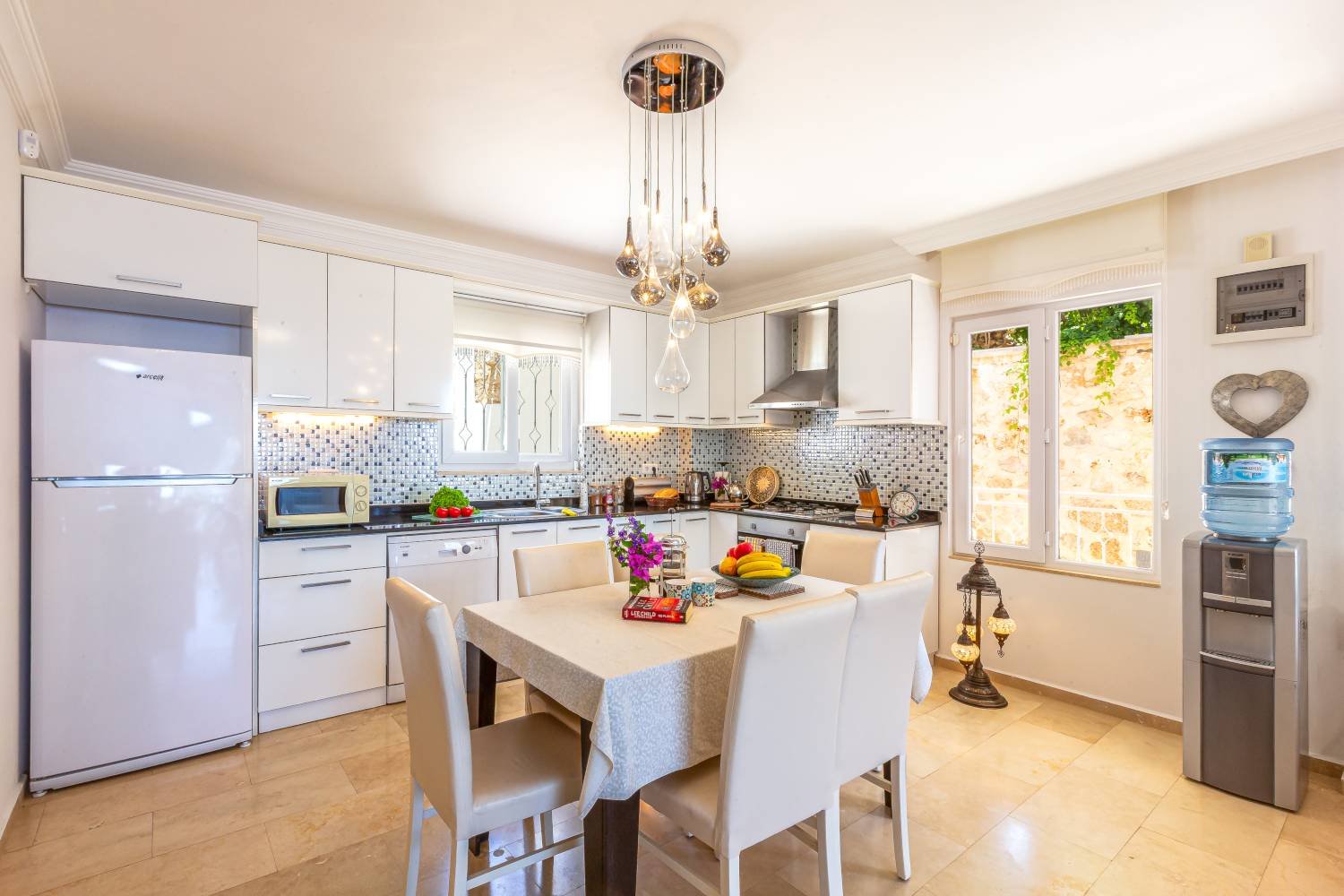Bright modern kitchen and dining area at Kalkan Limon Apartment with white cabinets, mosaic backsplash and a six‑seat dining table.