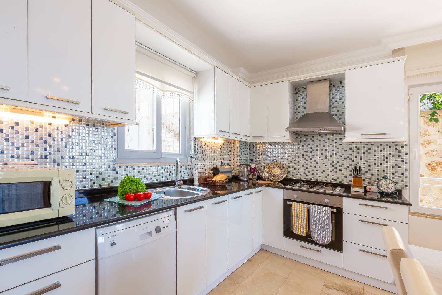 Modern kitchen at Kalkan Limon Apartment with white cabinets, mosaic tile backsplash and stainless‑steel appliances.