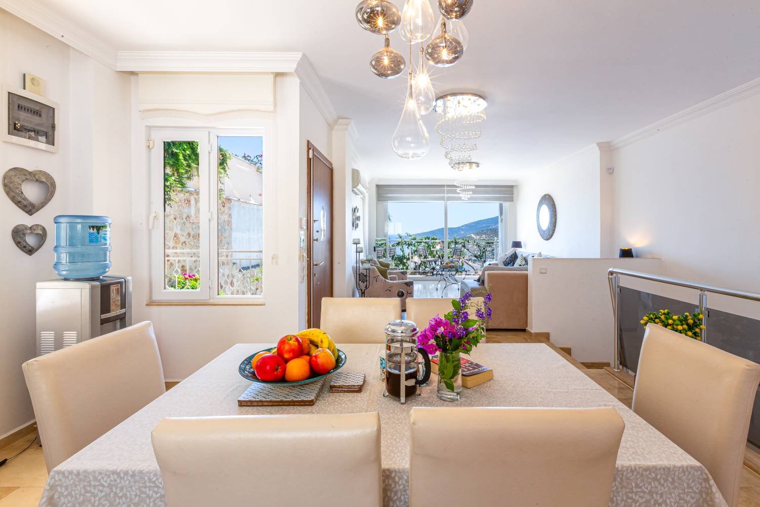 Bright dining and living area at Kalkan Limon Apartment with fruit bowl, French press and balcony mountain views.