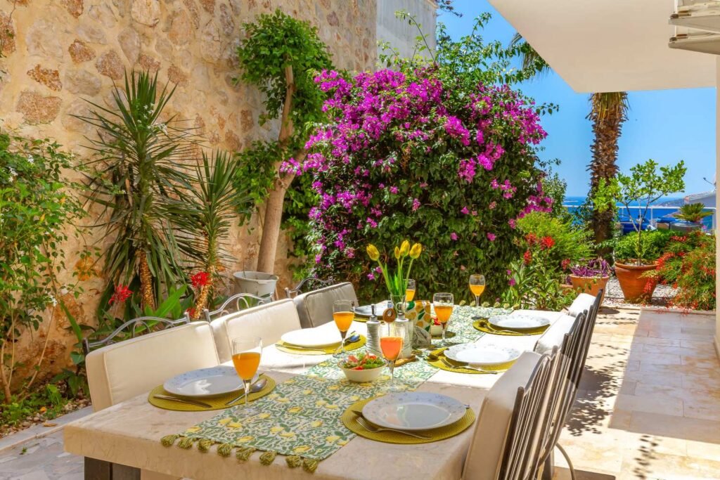 Outdoor dining table at Kalkan Limon Apartment with garden plants, sea view and colourful table settings.