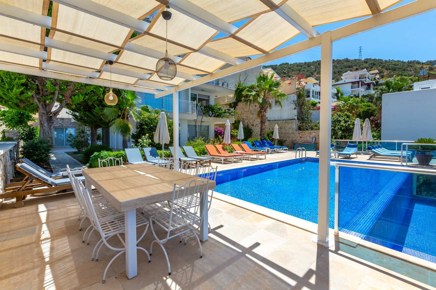 Outdoor pool area at Kalkan Limon Apartment with shaded dining terrace, sun loungers and lush greenery.