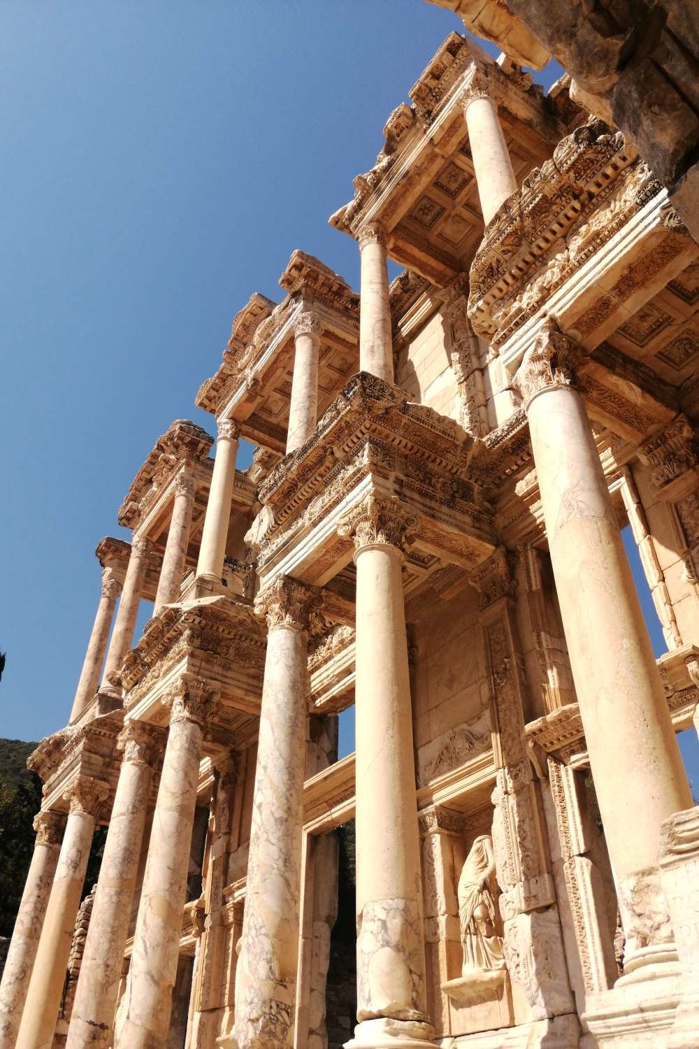 Detailed façade of the Library of Celsus in Ephesus with carved columns and ornate stonework under a clear sky.