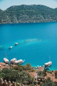 Turquoise Kekova bay with boats, hillside greenery and red‑roofed waterfront buildings near Kalkan.