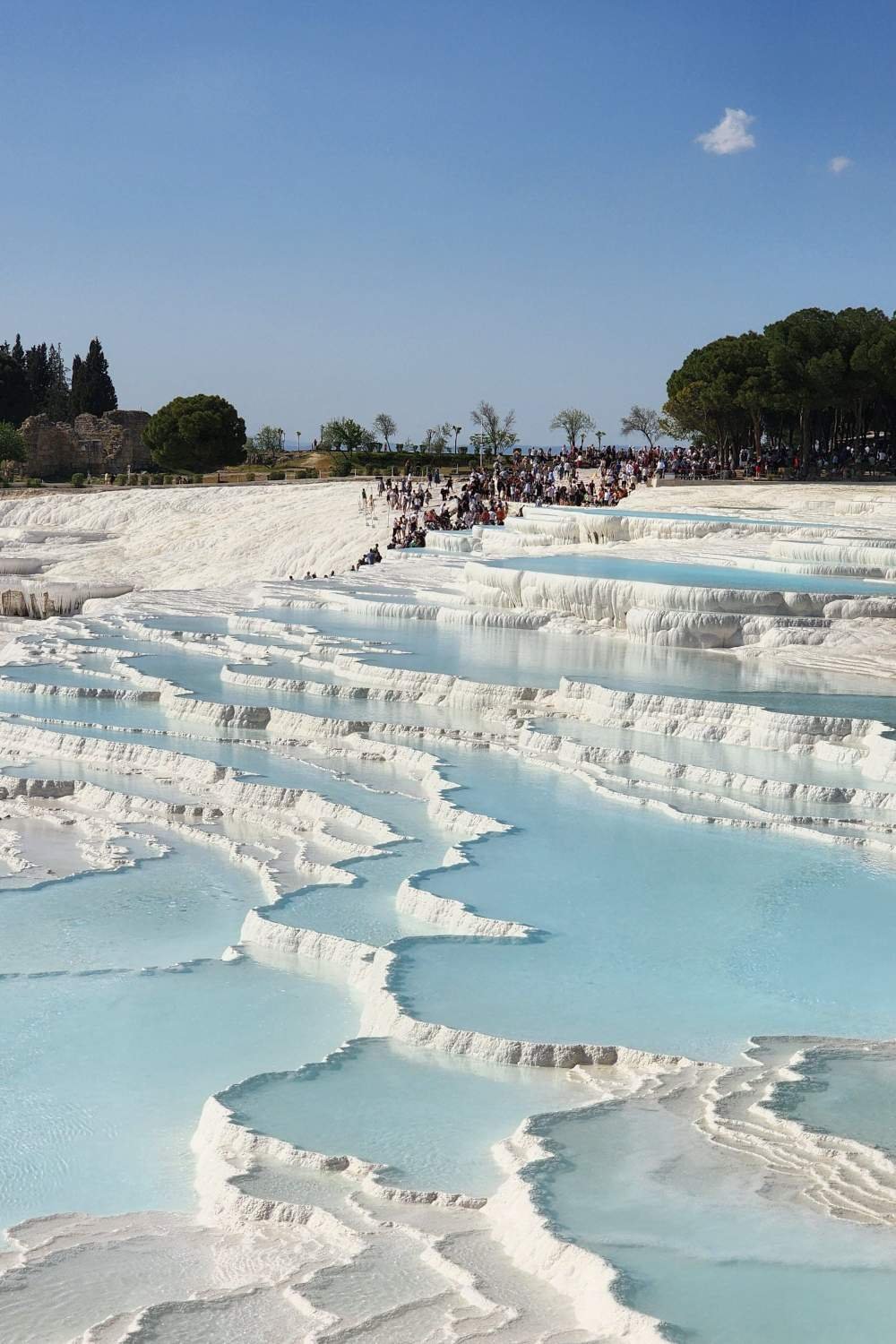 Pamukkale white travertine terraces with turquoise thermal pools and visitors exploring the site.