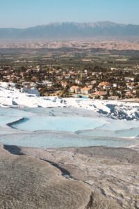 Pamukkale white travertine terraces with turquoise thermal pools overlooking the town and distant mountains.