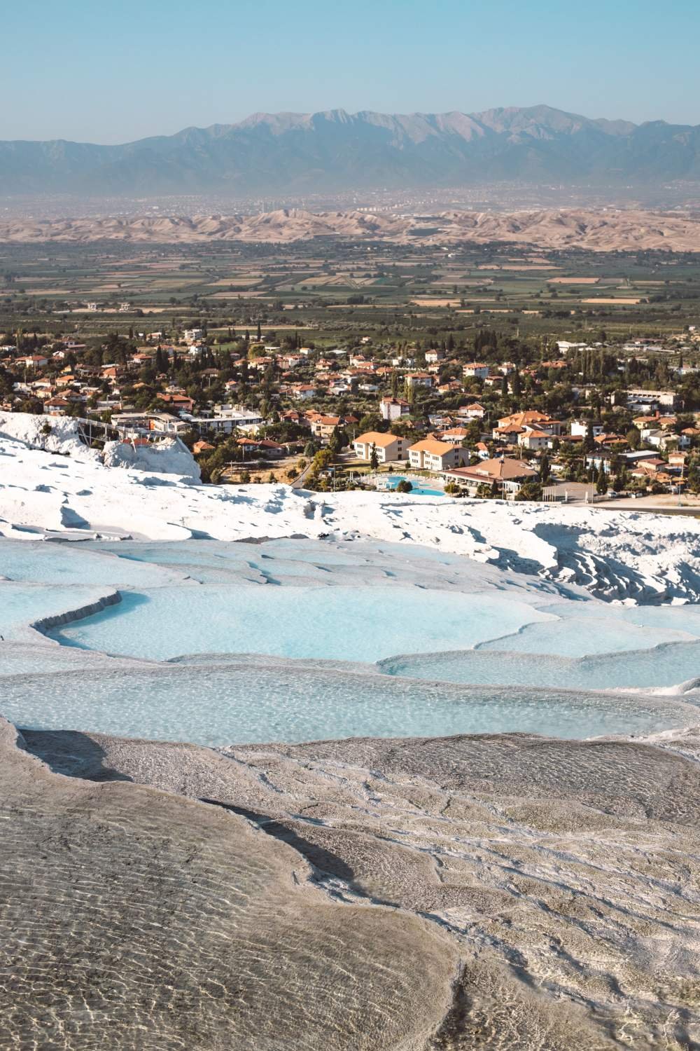 Pamukkale white travertine terraces with turquoise thermal pools overlooking the town and distant mountains.