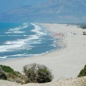 Wide sandy beach near Kalkan with deep blue sea, gentle waves and distant mountains.