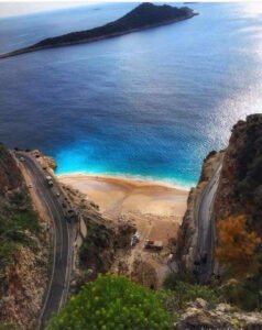 Turquoise beach near Kalkan with winding coastal road, rocky cliffs and clear blue sea.