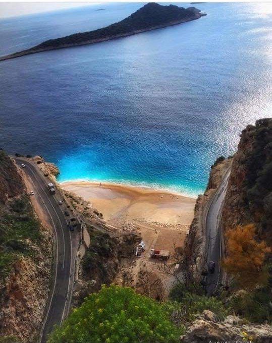 Turquoise beach near Kalkan with winding coastal road, rocky cliffs and clear blue sea.