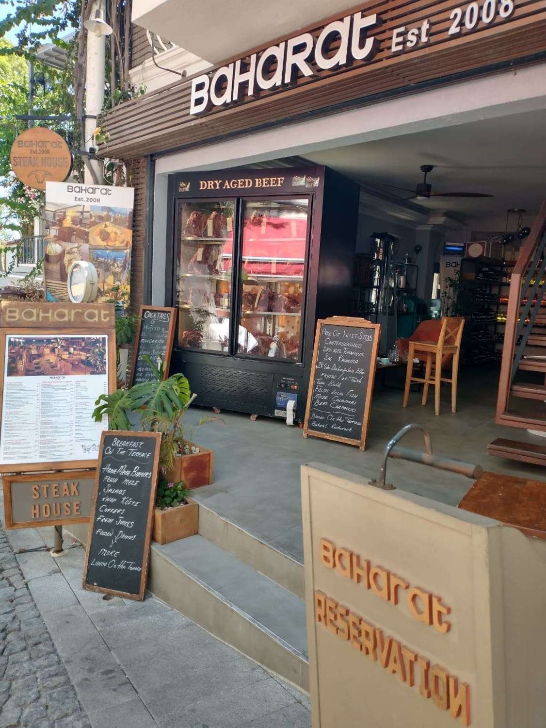 Exterior of Baharat Steak House in Kalkan with dry‑aged beef display, menu boards and terrace dining signs.
