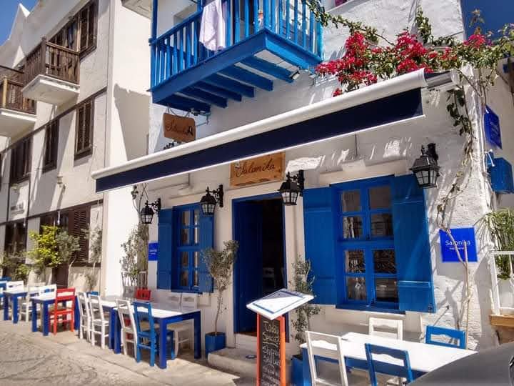Mediterranean‑style restaurant in Kalkan with blue shutters, outdoor seating and vibrant bougainvillea.