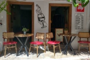 Outdoor seating area of a small café in Kalkan with wooden tables, red‑cushioned chairs, Illy coffee signage and a visible drinks menu.