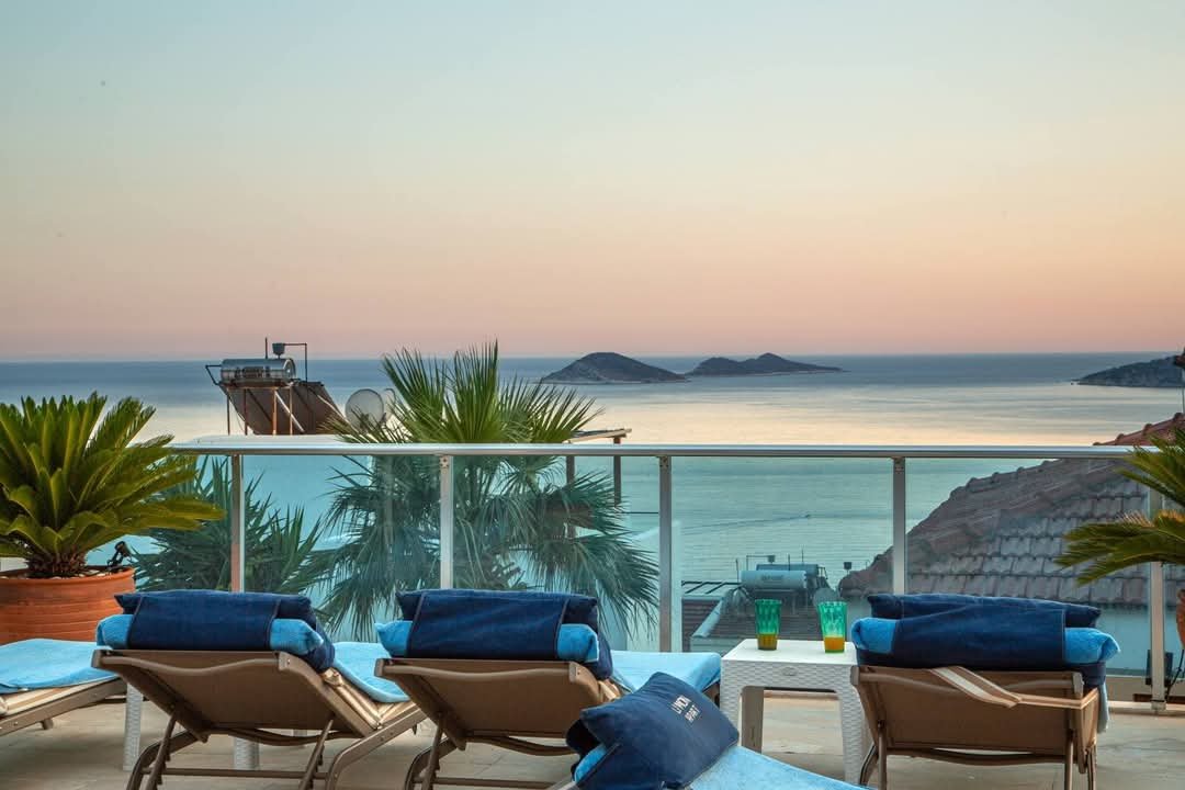Sunset terrace at Kalkan Limon Apartment with blue loungers, glass railing and sea view.