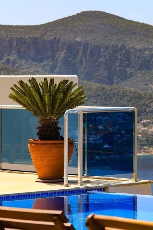 Poolside view at Kalkan Limon Apartment with terracotta plant pot, glass railing and sea‑and‑mountain backdrop.