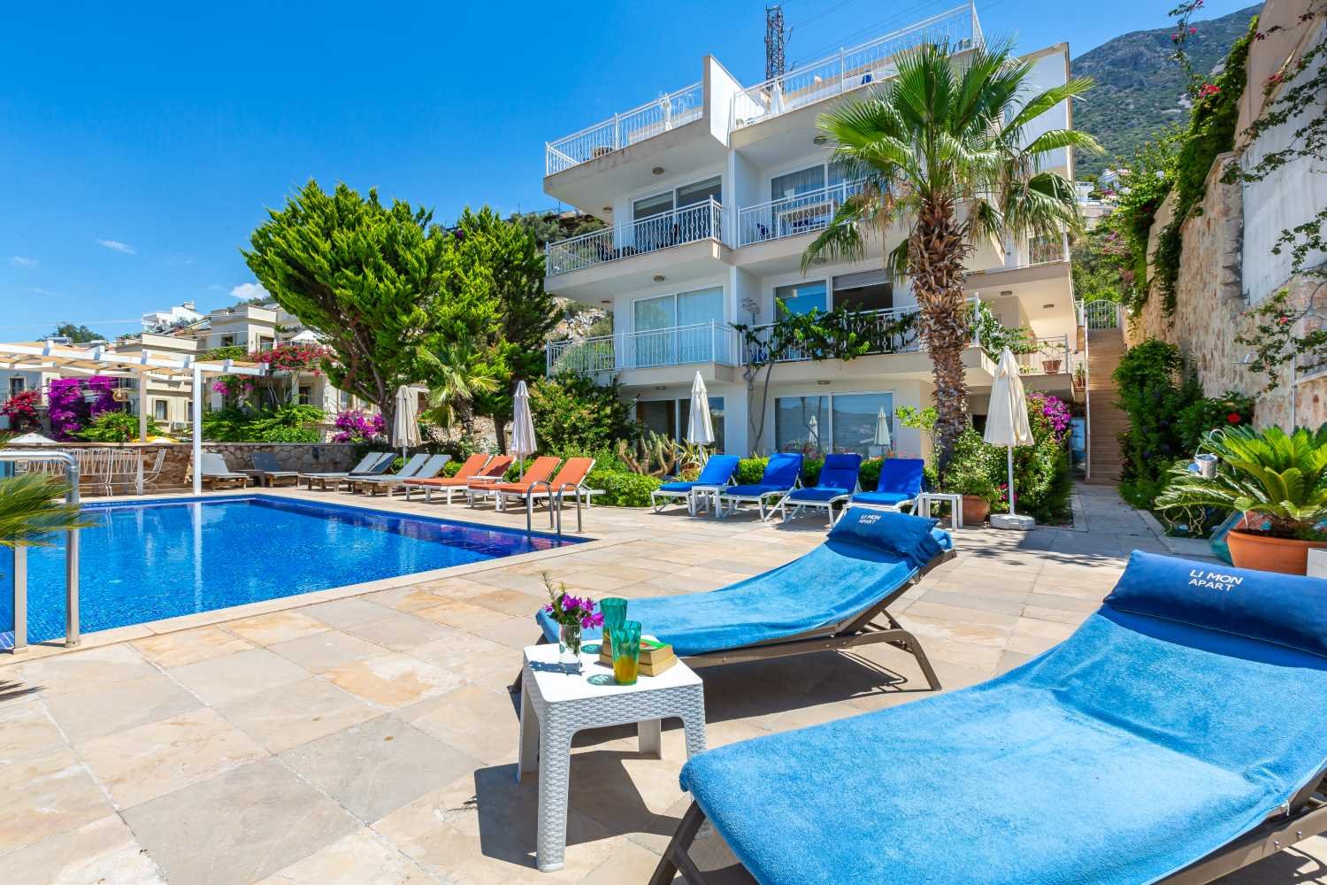 Poolside loungers at Kalkan Limon Apartment with clear blue water, garden views and modern outdoor seating.