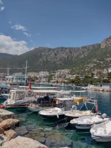 Kaş harbour with small boats, clear turquoise water and hillside town beneath rugged green mountains.