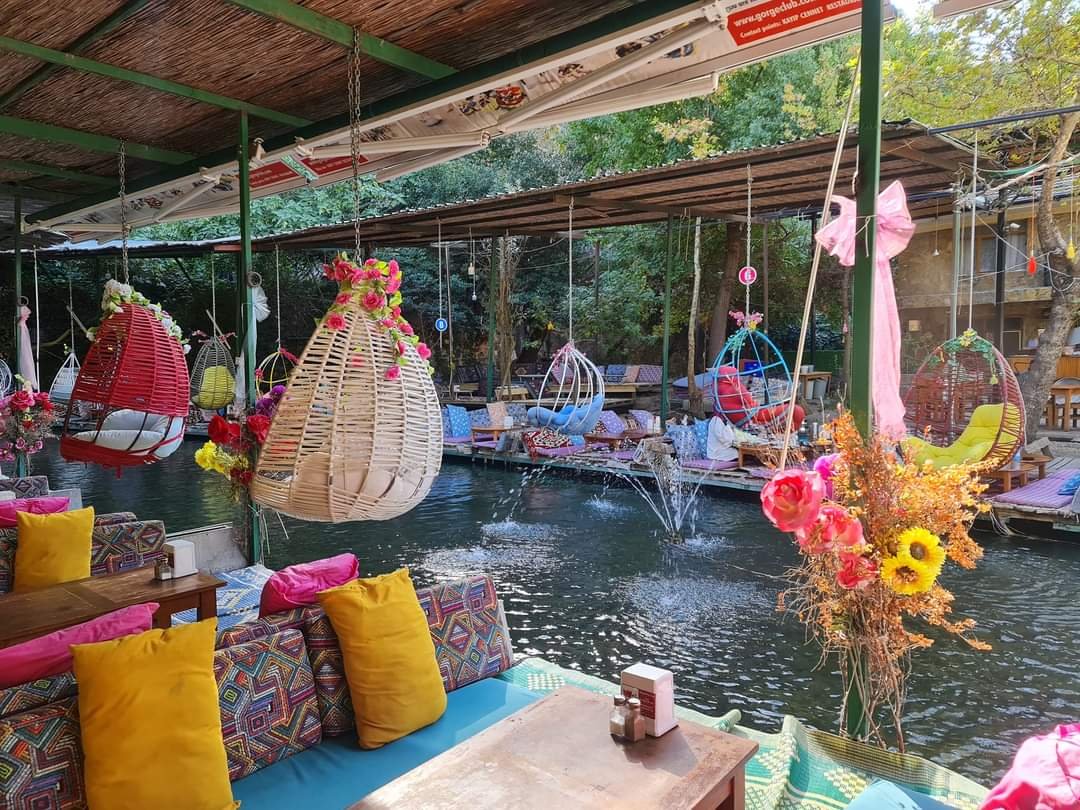 Colourful riverside seating area at Saklıkent with hanging wicker chairs, fountains and vibrant décor.