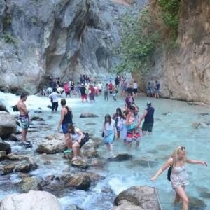 Visitors walking through shallow blue water between steep rocky cliffs at Saklıkent Gorge near Kalkan.